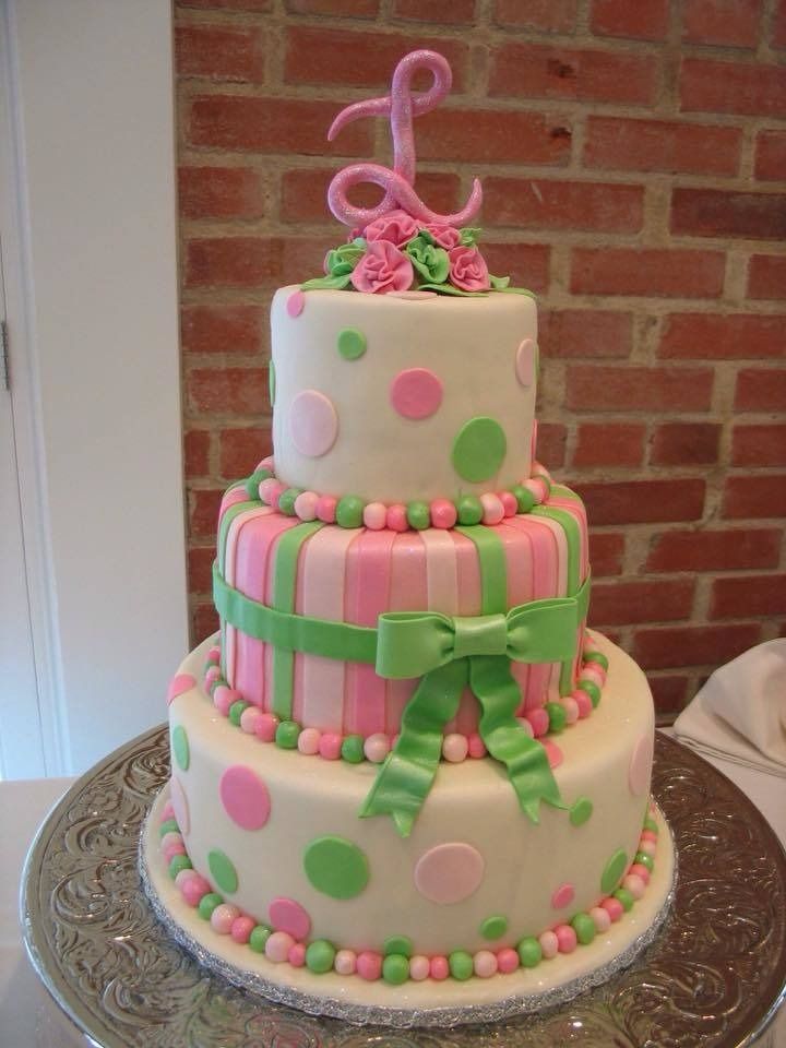 Three-tier pink and green polka-dot cake with bows and floral decorations on a table