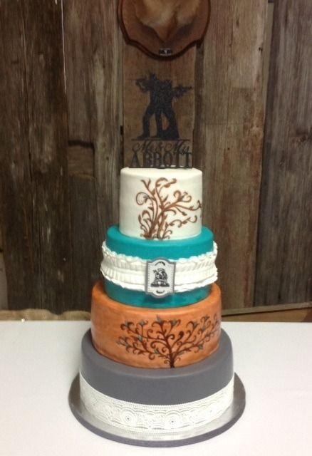 Four-tier wedding cake with white, teal, orange, and gray layers on a table