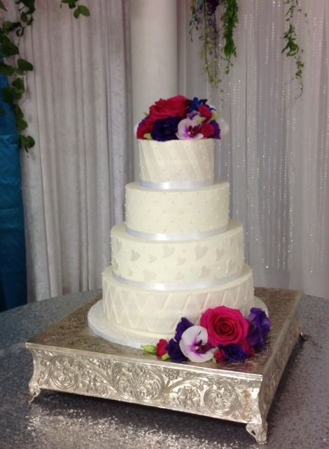 White tiered wedding cake with purple and pink flowers on a silver stand