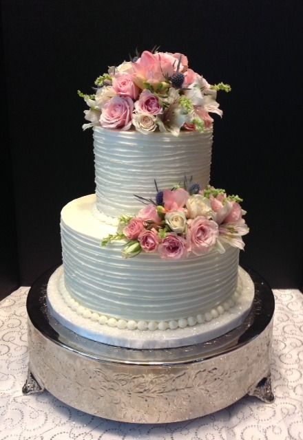 Two-tier white cake with pink flowers on a silver stand against a black background