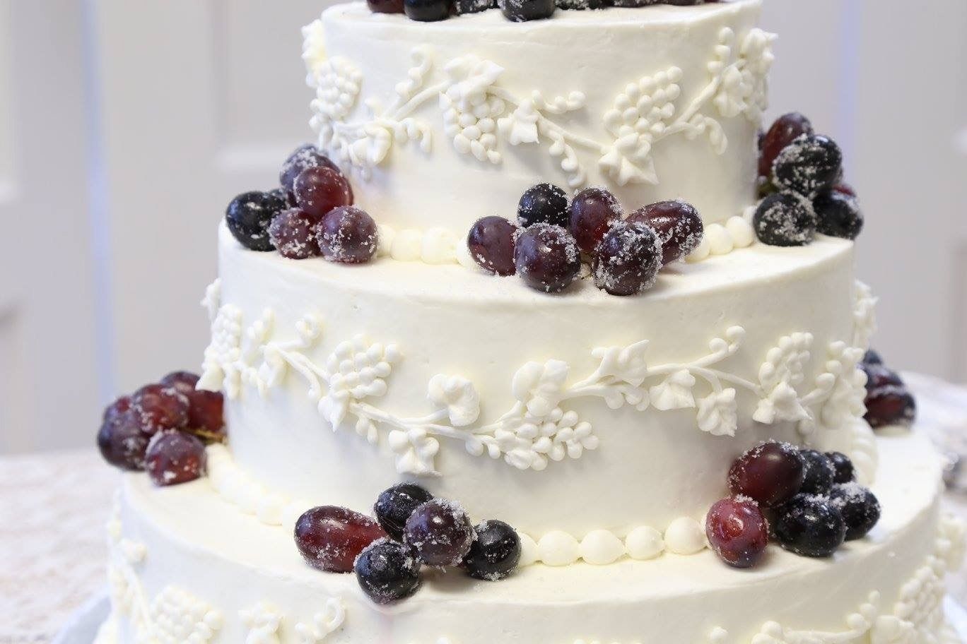White tiered cake decorated with white frosting flowers and dark berries on each layer