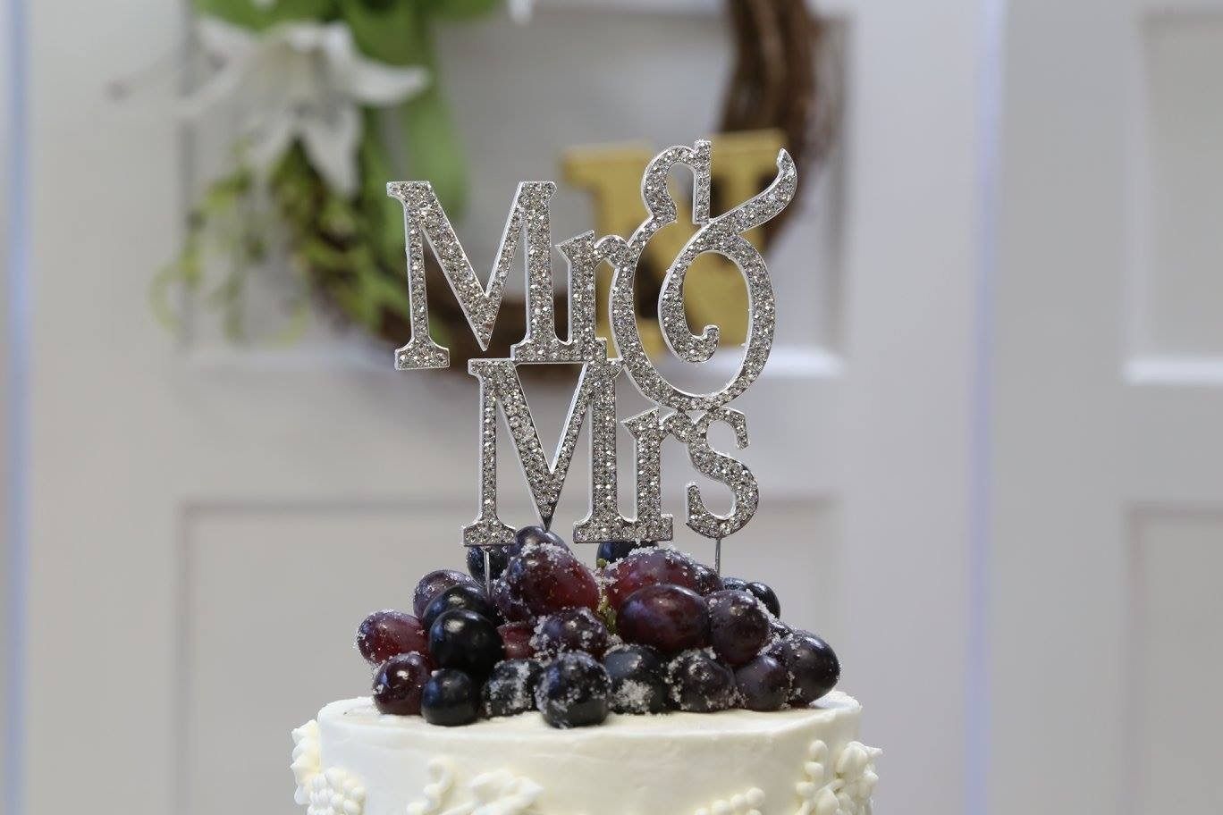 Sparkling “Mr & Mrs” cake topper on a white frosted cake topped with dark berries