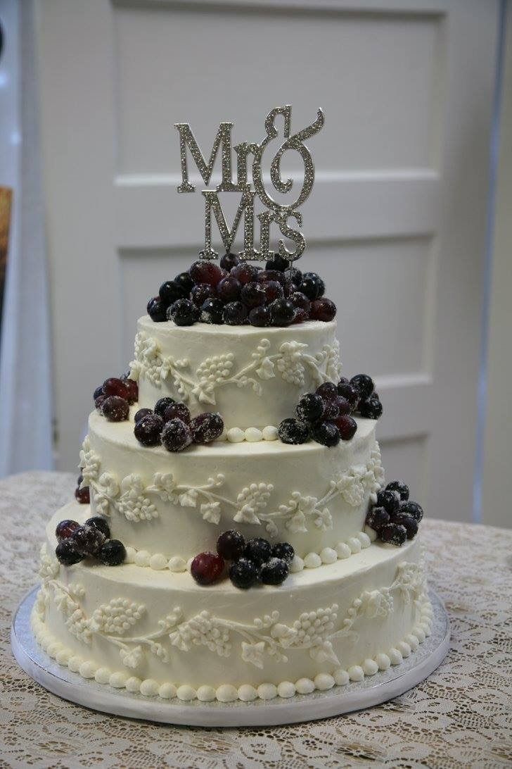 White tiered wedding cake with berries and a gold “Mr & Mrs” topper