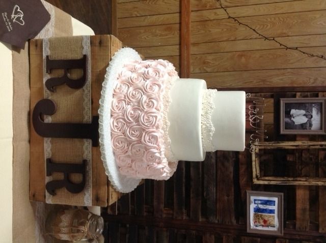 Two-tier pink and white rose cake on a rustic wooden display stand