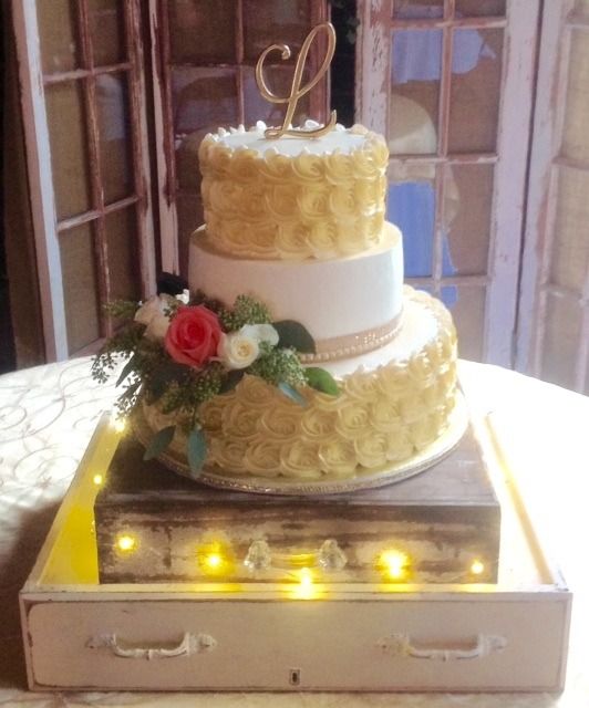 Elegant white-and-yellow tiered cake with flowers and lit candles on a wooden stand