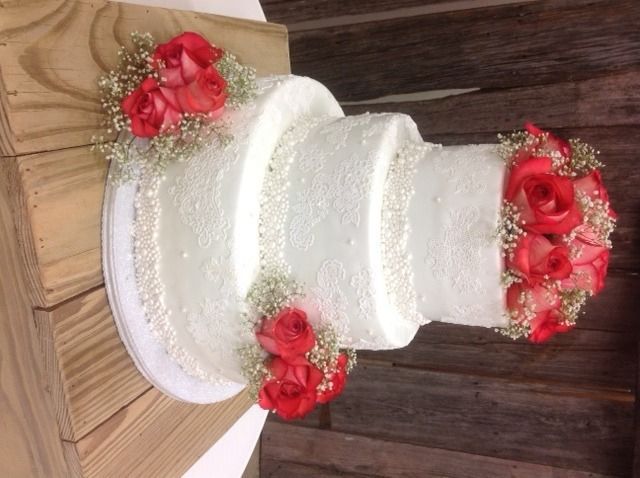 White tiered cake decorated with red flowers on a wooden table