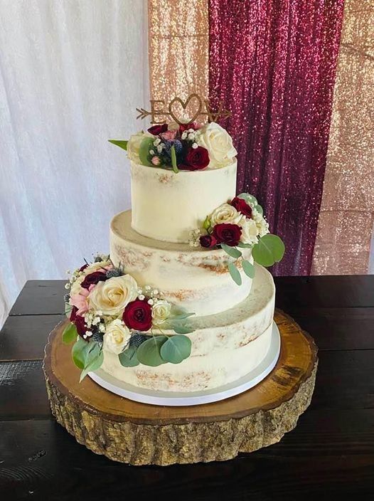 Three-tier white wedding cake with burgundy and cream flowers on a gold stand against a glittery backdrop