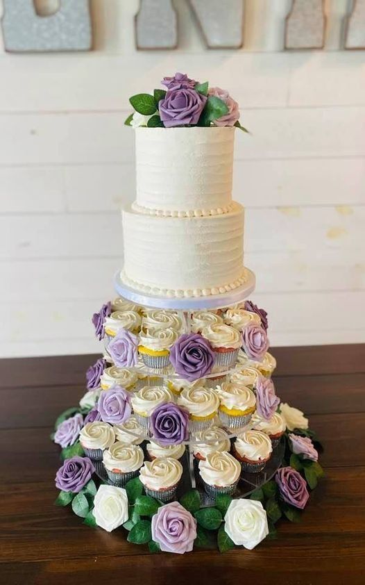 White tiered wedding cake with purple and cream roses cascading around the base and top