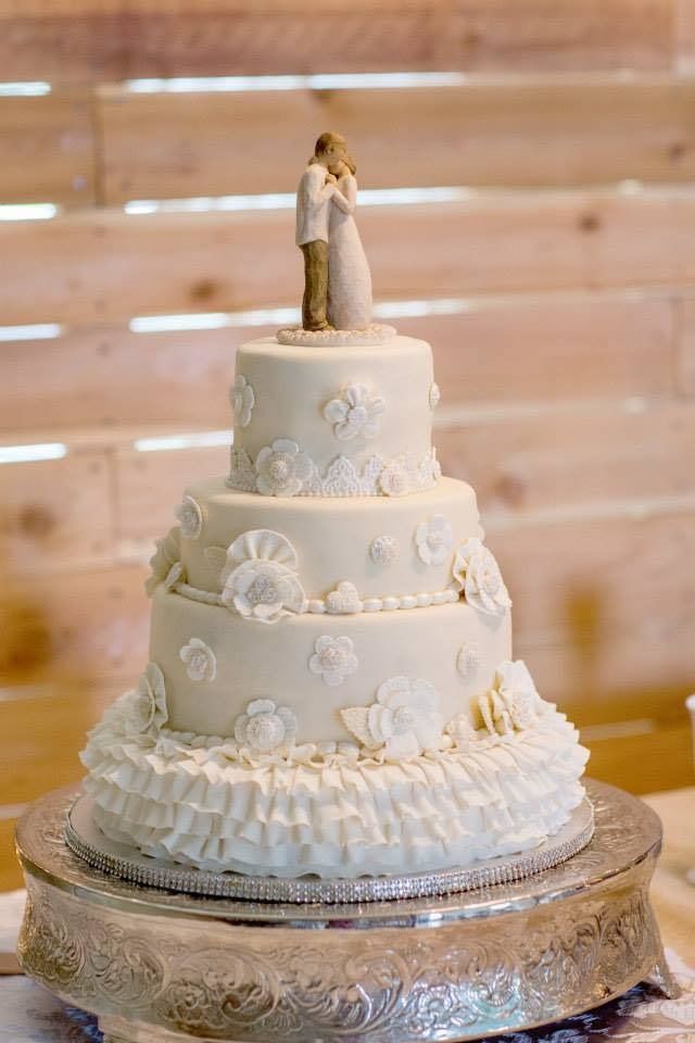 Three-tier white wedding cake with floral decorations and a bride-and-groom topper on a silver stand