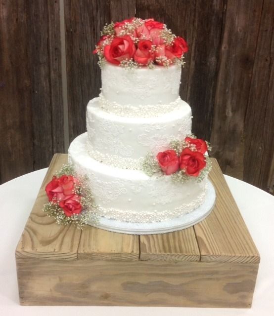 Three-tier white cake with red flowers on a wooden stand