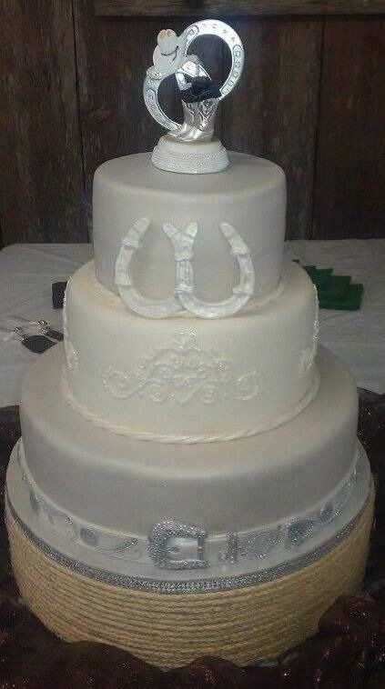 Four-tier white wedding cake with silver horseshoe and glittery topper, decorated with delicate white details