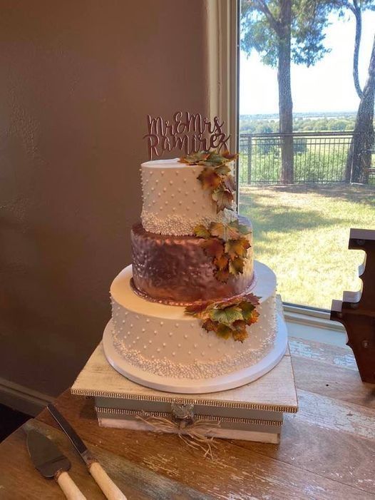 Two-tier rustic white and brown wedding cake on a table by a window with floral accents