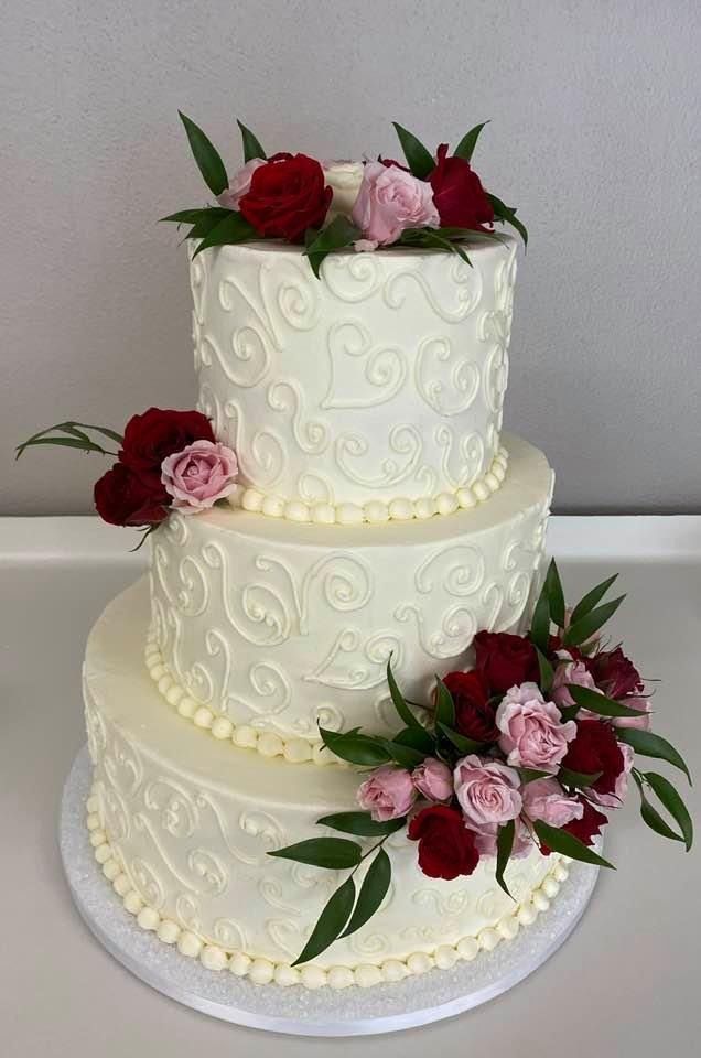 Three-tier white wedding cake with red and pink flowers and green leaves