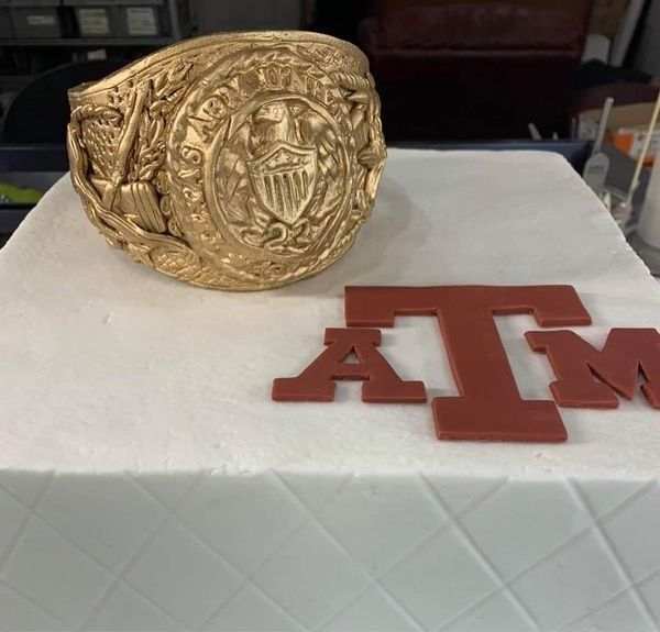 Gold championship ring beside a red Texas A&M logo on a white cloth.