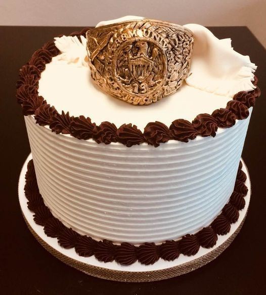 White frosted cake with chocolate trim and a gold decorative topper on a cake board