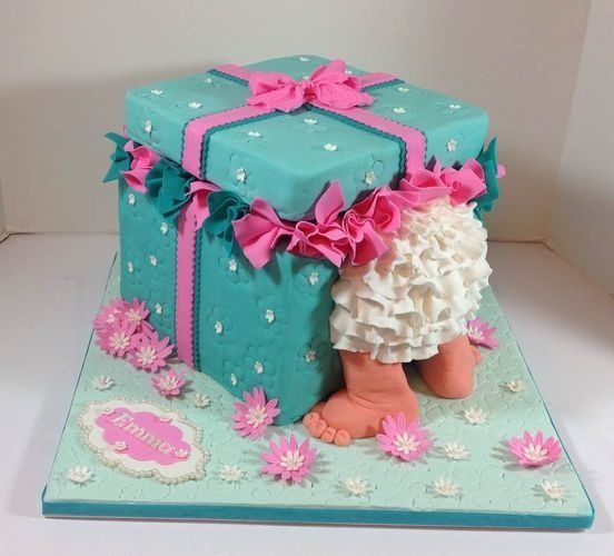 Teal gift box cake with pink ribbons and flowers, topped with white frilly accents on a matching base.