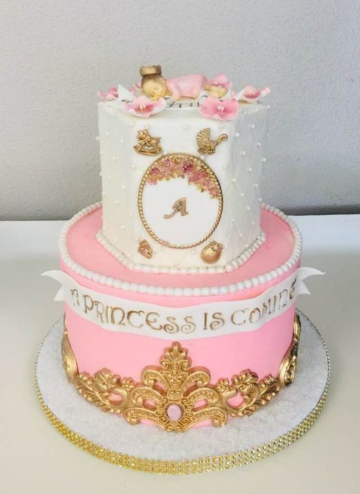 Pink and gold princess-themed two-tier cake with crown decorations and an “A” monogram