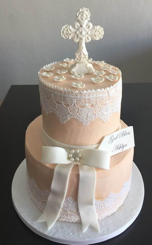 Elegant two-tier peach and white cake with lace details and a pearl cross topper on a white base