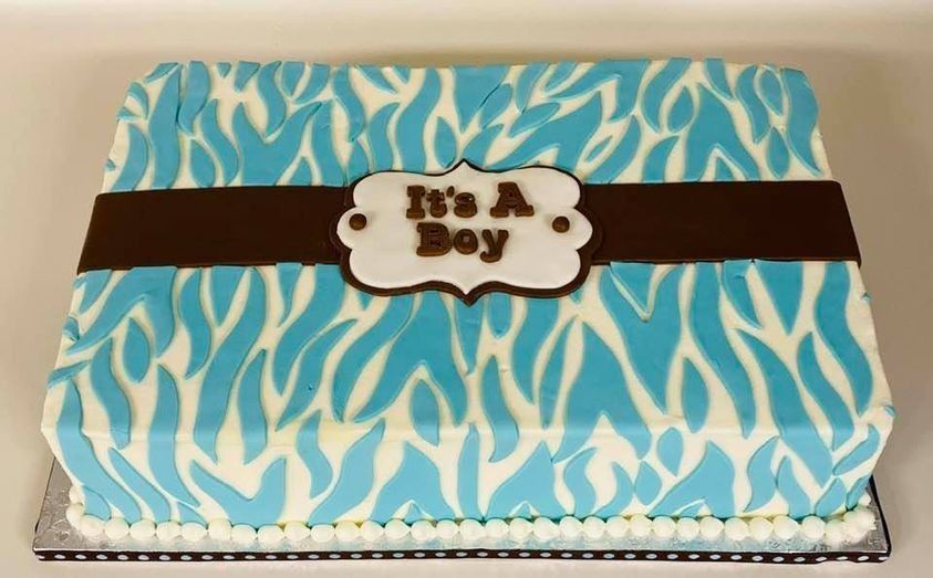 Baby shower cake with blue-and-white feather design and a brown ribbon reading “It’s a Boy”