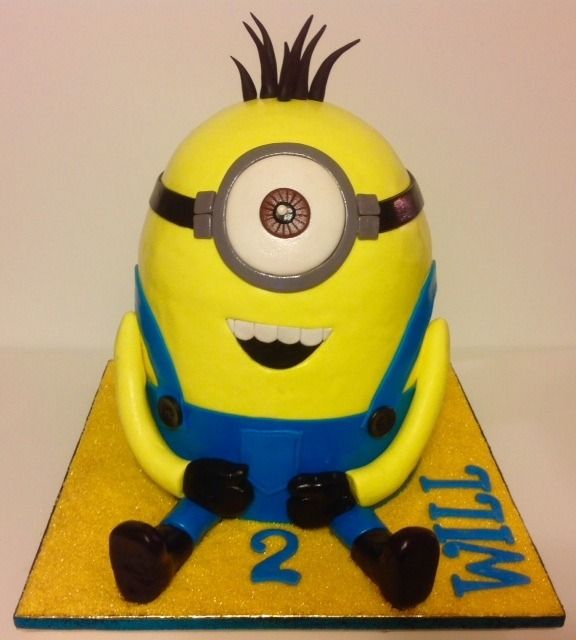 Minion character cake with blue overalls, sitting on yellow base with “2” and “Will”