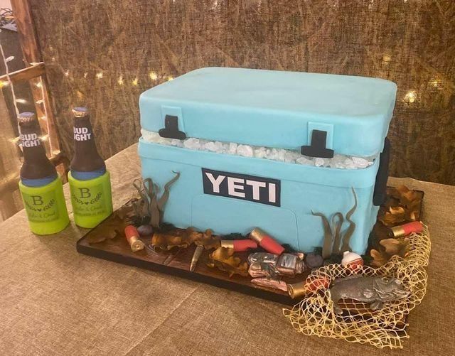 Blue YETI cooler with fishing gear and two bottles on carpeted floor, rustic indoor setting