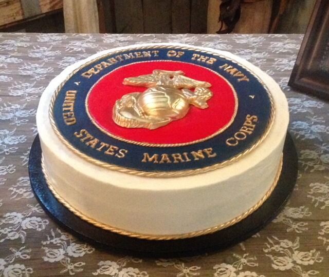 Round white cake with a U.S. Marine Corps emblem on top, set on a patterned tablecloth
