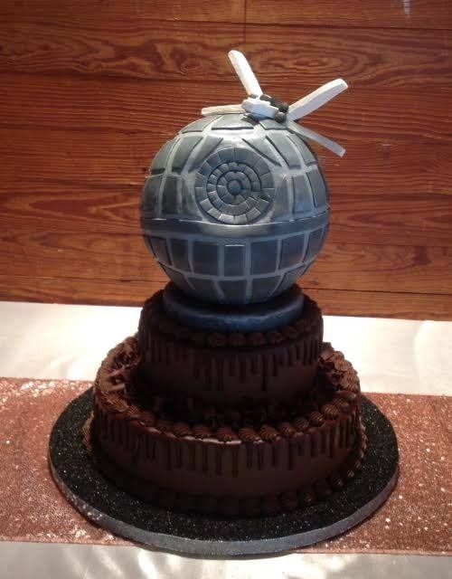 Gray spherical sci-fi prop cake on a dark tiered base, with small white antennae against a wooden wall.