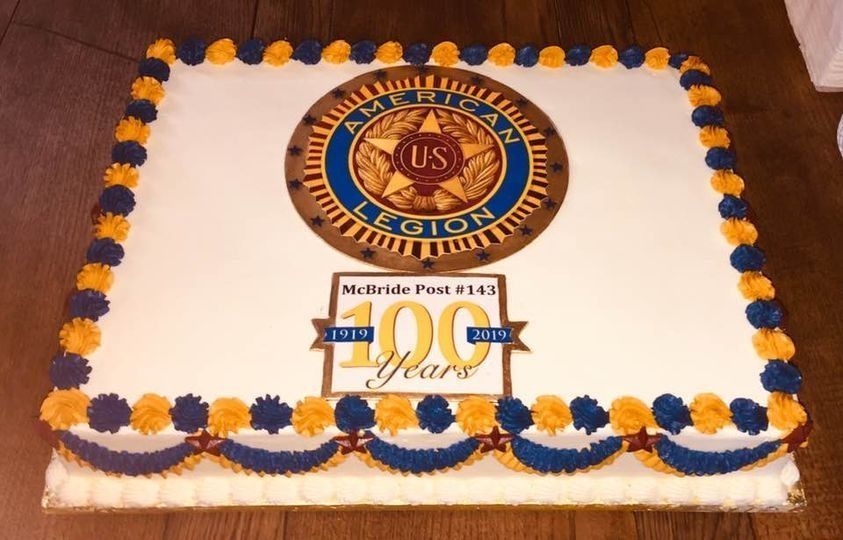 White square cake with blue and orange frosting border and a central US naval emblem on a wooden table