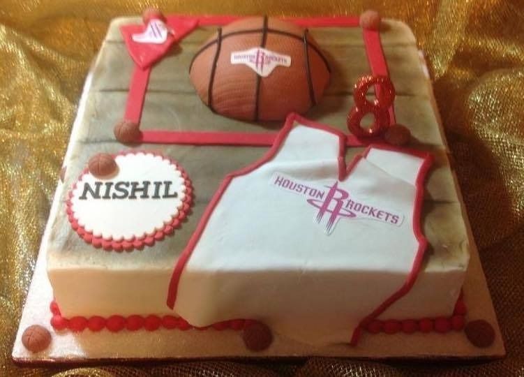 Basketball-themed cake with Houston Rockets logo, hoop, and the name NISHIL on white frosting