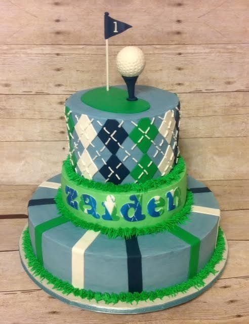 Two-tier green, blue, and white cake with a golf ball topper and small flag reading “Ryder”