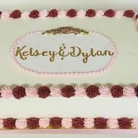 Pink and white cake with gold script reading “Kelsey & Dylan” and decorative frosting borders