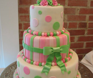 Three-tier pastel pink and green polka dot cake with ribbon trim and bow on a table