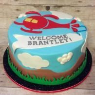 Blue cake with a red helicopter and “WELCOME BRANTLEY” text on top