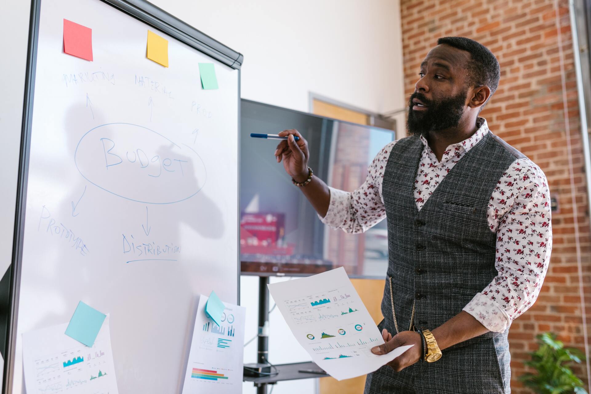 Man presenting at whiteboard, pointing to notes. In office setting.