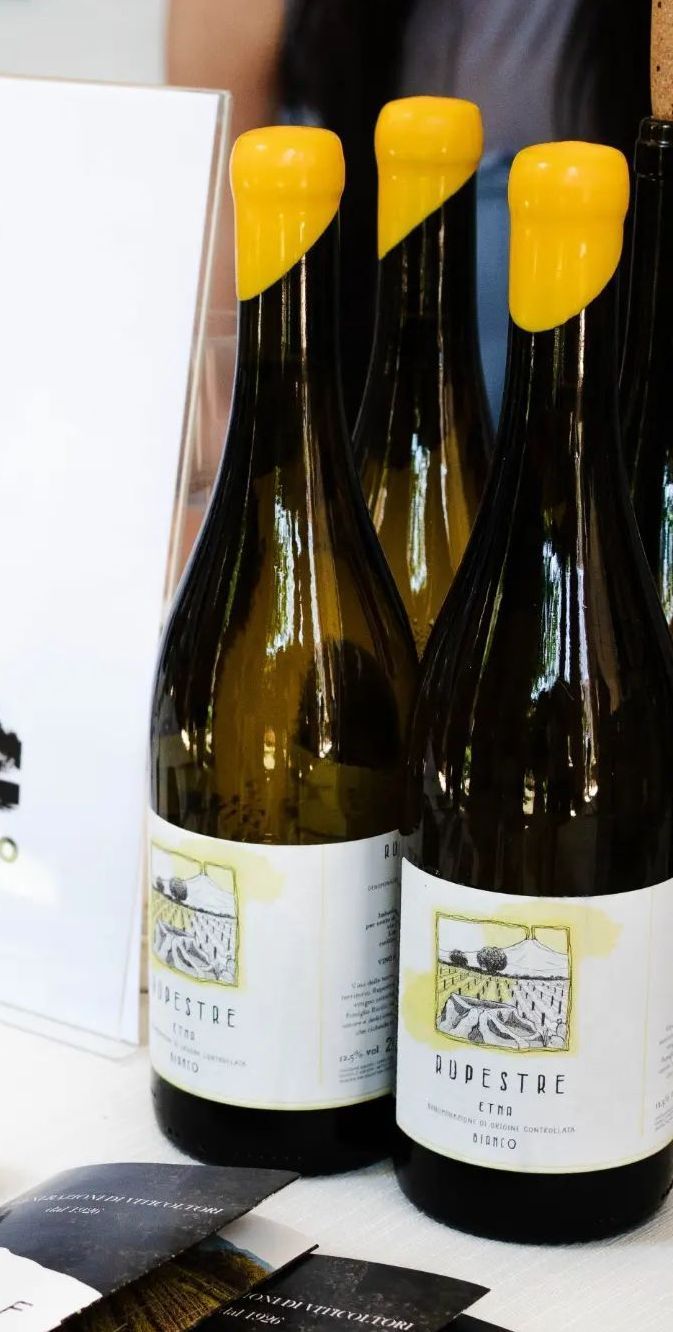 Bottiglie di vino con tappi di alluminio giallo ed etichette bianche, primo piano.