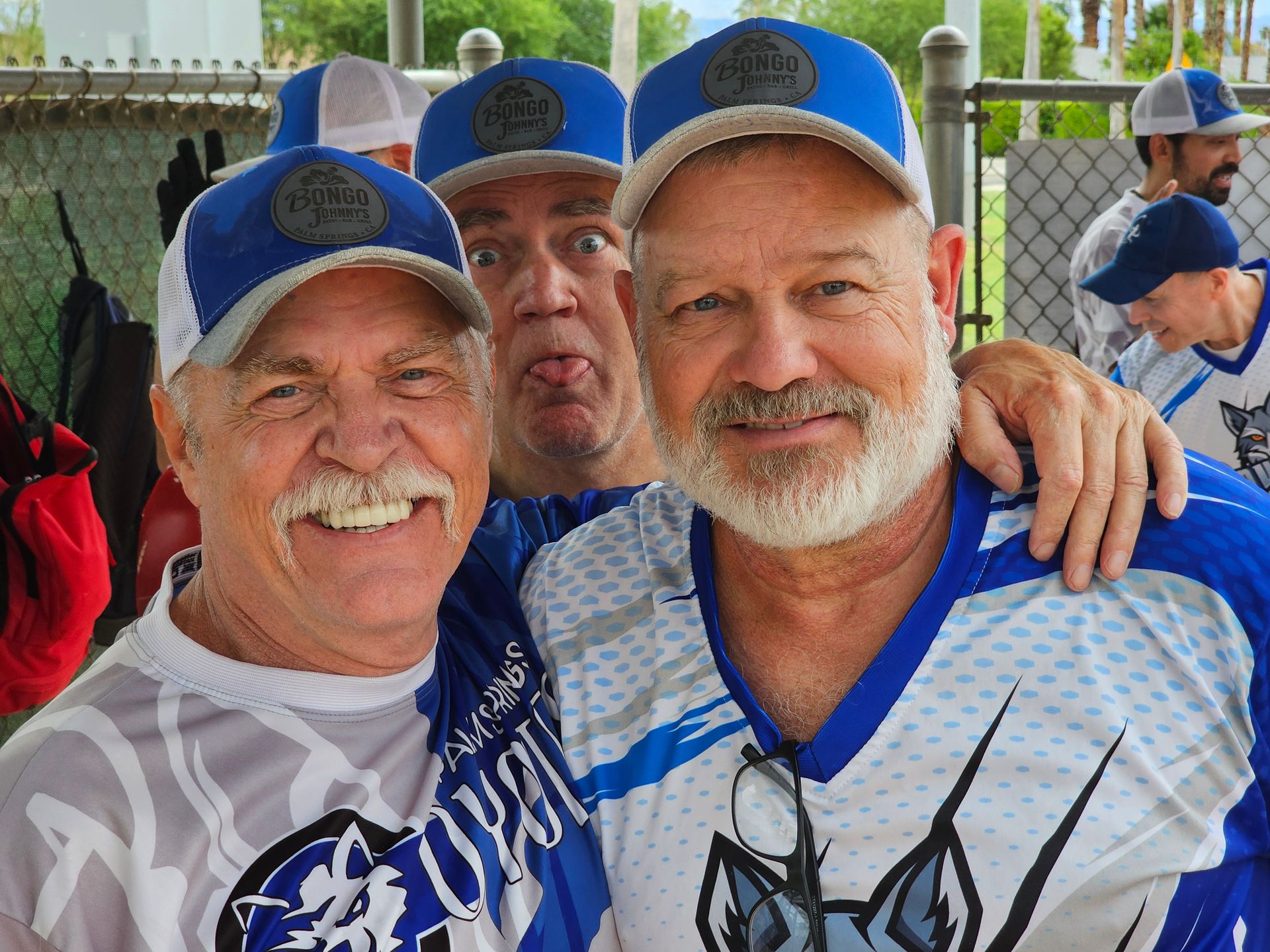 Three smiling baseball fans in blue caps and jerseys posing together outdoors