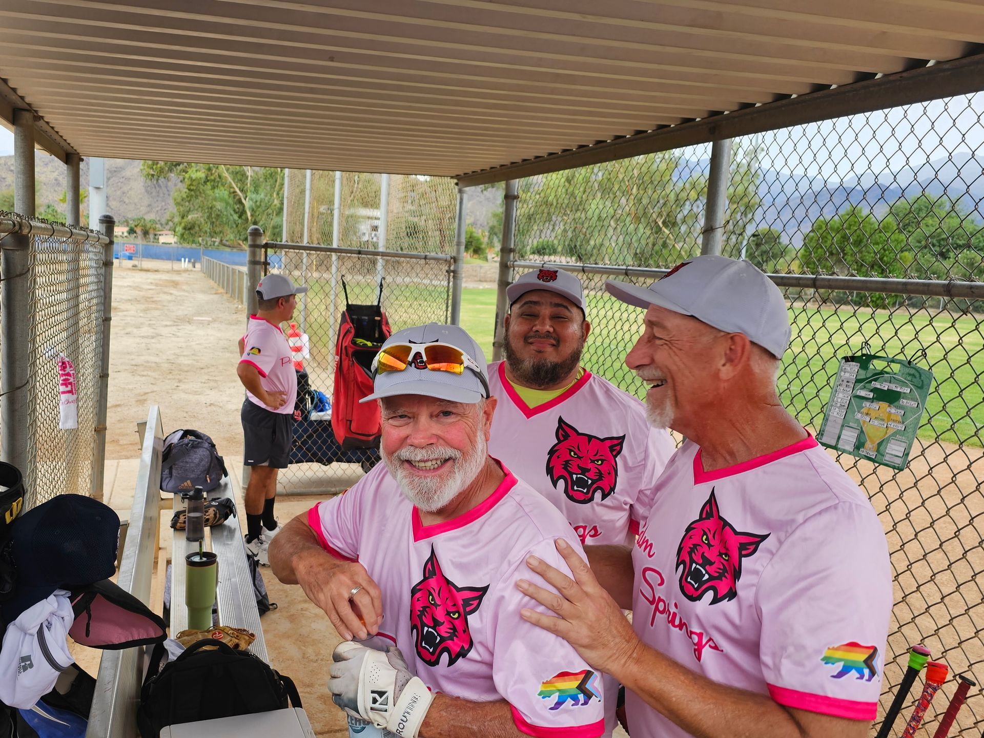 Two men in white and pink jerseys smile under a pavilion at a field event