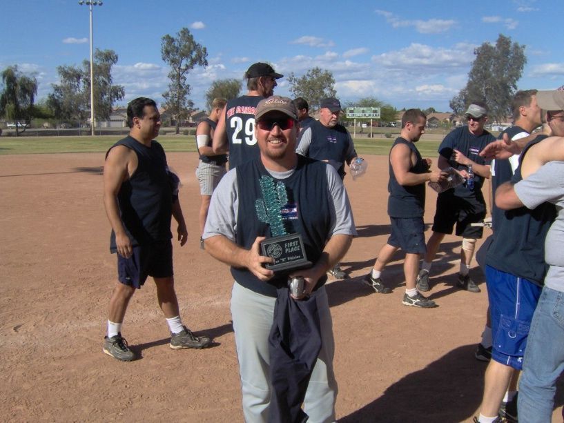 Group of people posing in sports uniforms on a baseball field under a clear sky