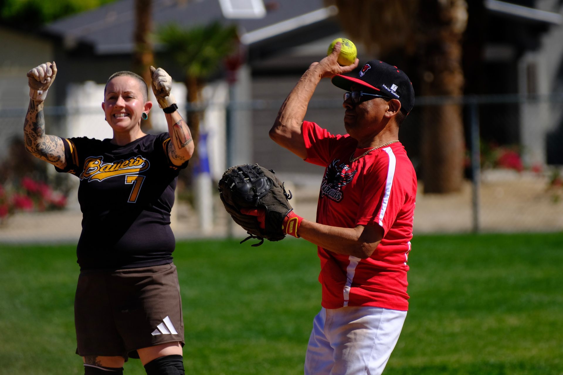 Two softball players in red and black uniforms celebrating on a grassy field
