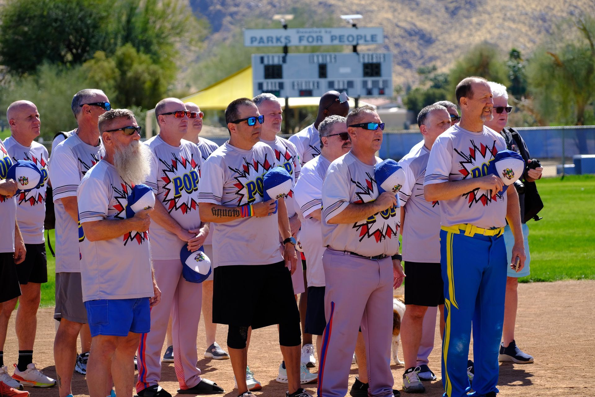 Group of people in matching shirts standing outdoors near a baseball field scoreboard