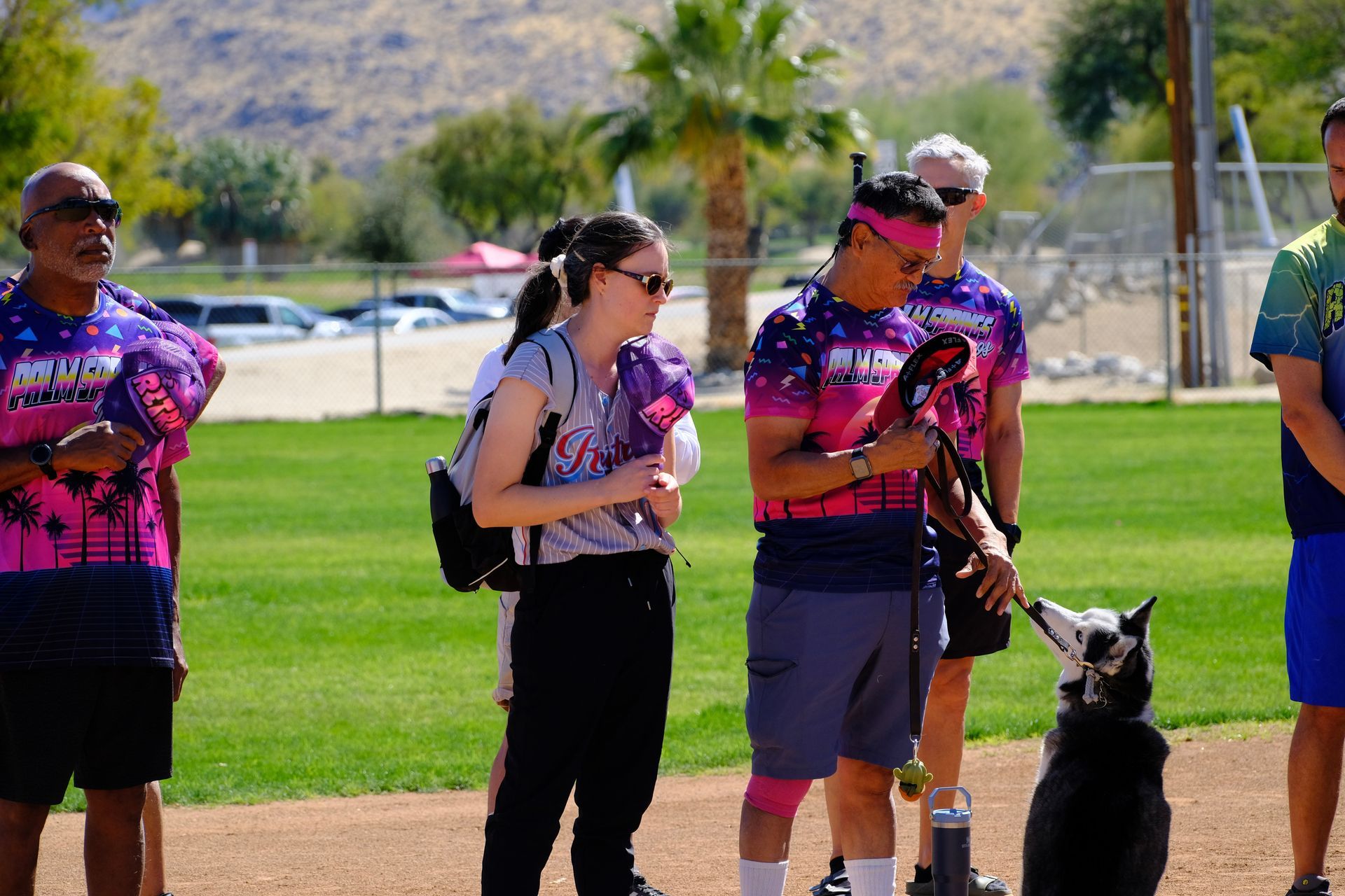 People in pink shirts stand on a grassy field with dogs during an outdoor event.