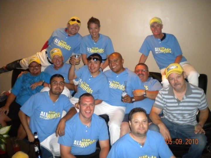Group of people in blue shirts and yellow caps posing together indoors, smiling at the camera.