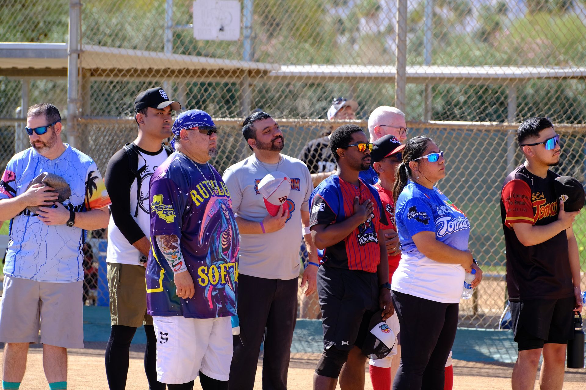 Group of softball players standing in a line on a sunny field, wearing colorful jerseys and caps