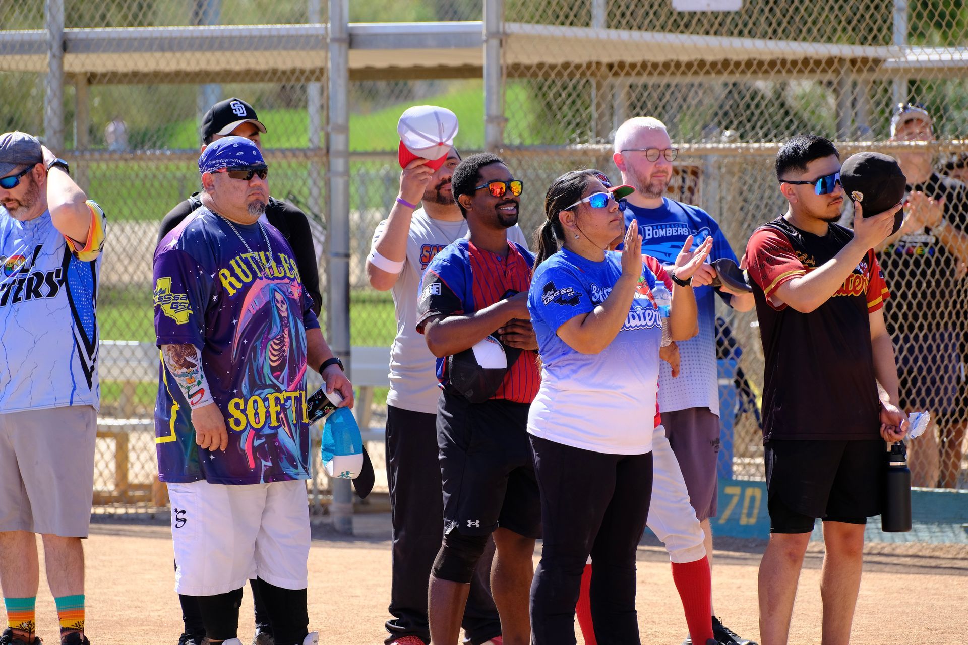 People standing in a line on a softball field, many holding bats and wearing jerseys and caps.
