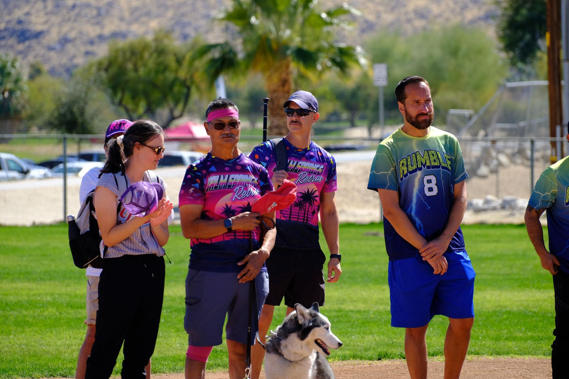 People standing on a grassy field with a dog, mountains in the background