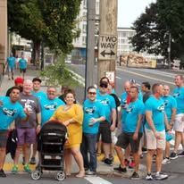 Group of people in turquoise shirts gathered on a city sidewalk, with one person pushing a stroller.