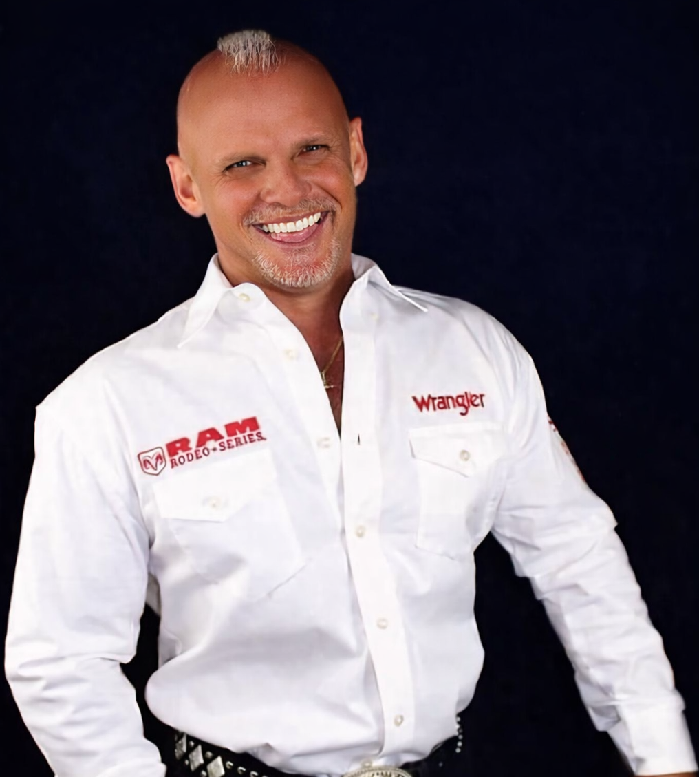 Smiling bald man in a white Wrangler shirt against a dark background
