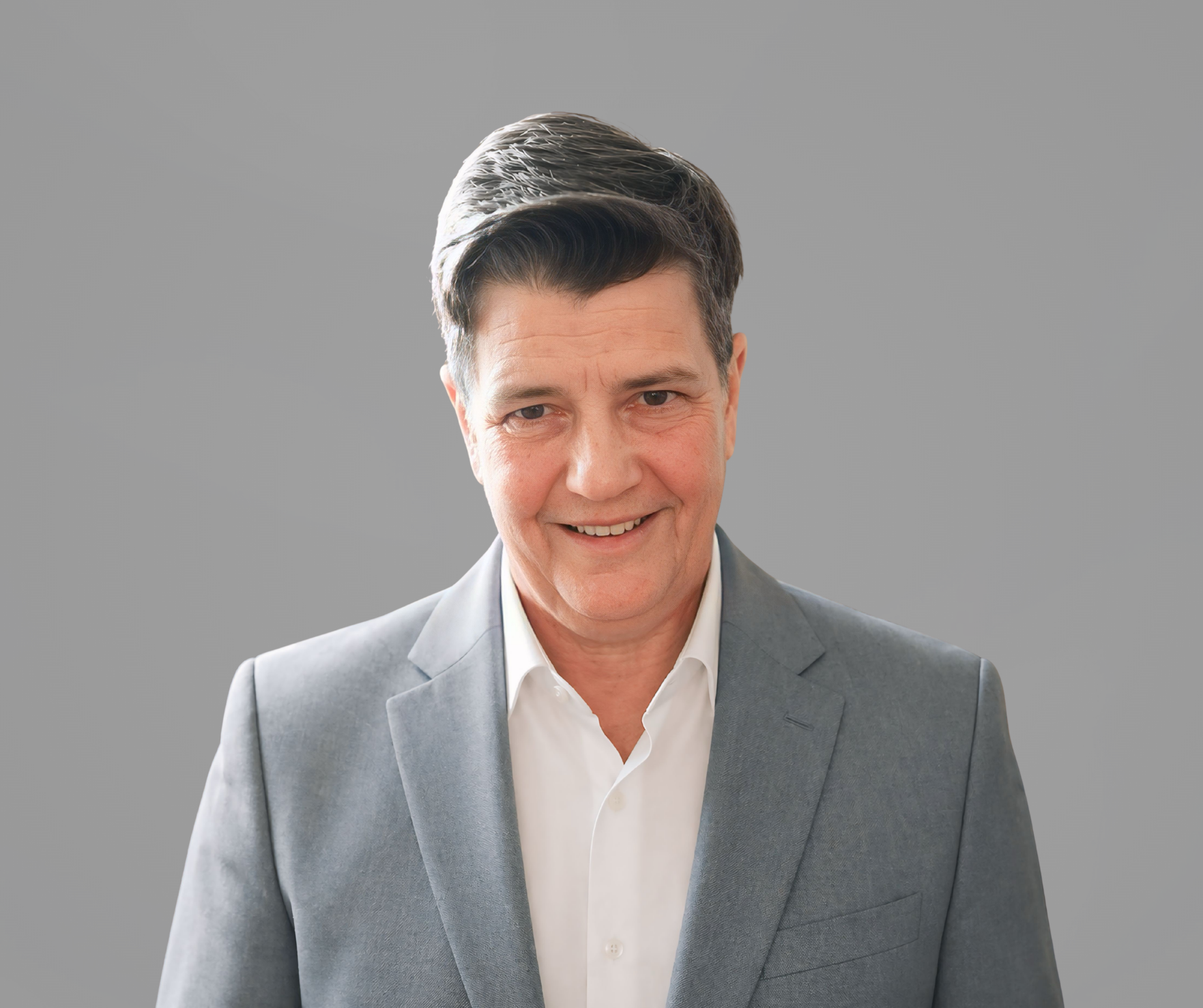 Headshot of DL Stanley, a woman smiling, wearing a white blouse and a gray jacket, set upon a gray background.