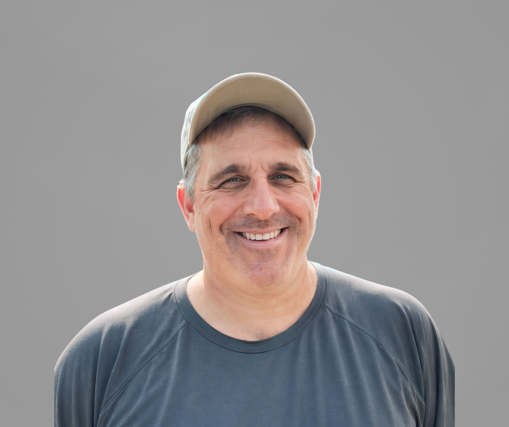 Headshot of Rick Kulek, a man smiling, wearing a baseball cap and a gray T-shirt, set upon a gray background.