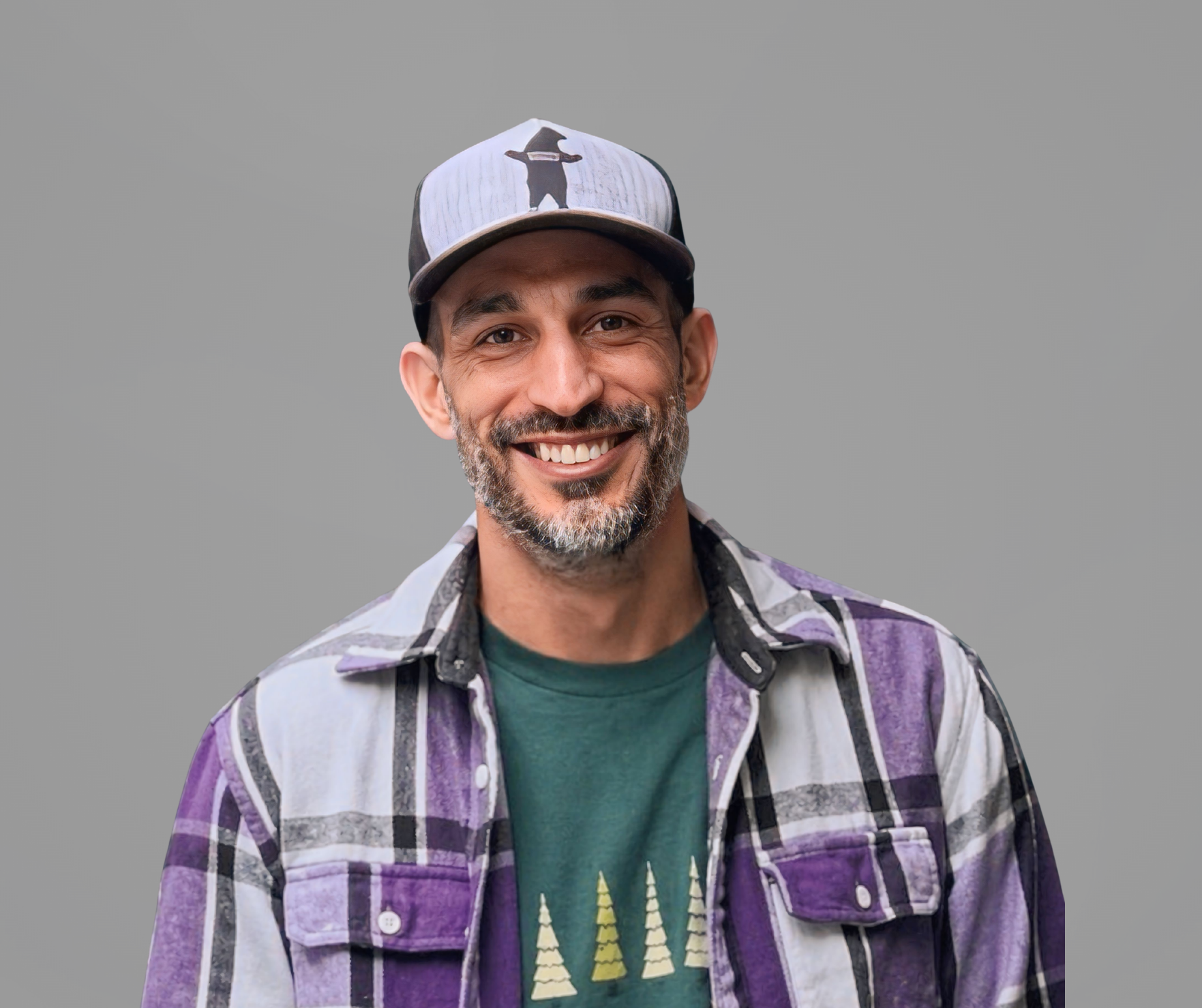 Smiling man in a purple plaid shirt and cap against a gray background